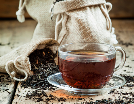 Black ceylon cup of black tea and dry tea in bags on the background of scattered tea leaves on the old wooden background, selective focus